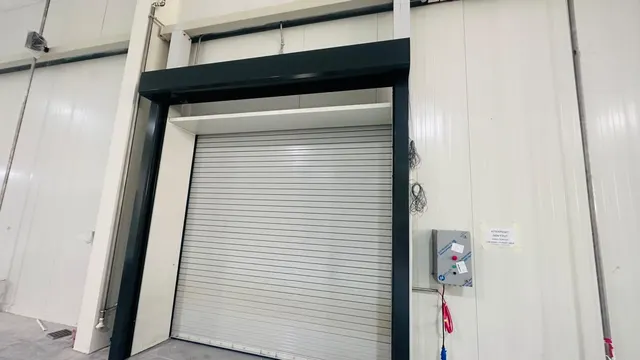 Motorised light grey rolling shutter in a dark charcoal steel frame with a wall mounted control panel at Al Hamra Port, Ras Al Khaimah